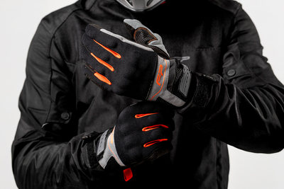 Motociclista ajustando guantes Core negros con detalles naranja, ventilados y ergonómicos para moto
