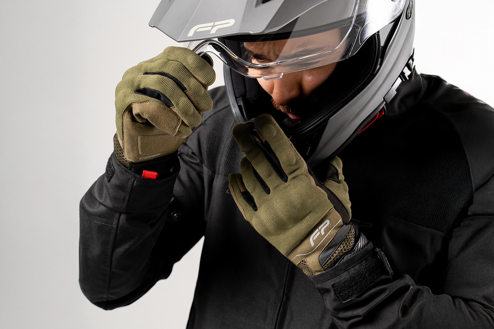 Motociclista con casco colocándose guantes Core verde militar ventilados, ideales para climas cálidos