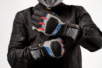Motociclista ajustando guantes impermeables Maverick Gris con membrana Hipora y protecciones para turismo en moto.