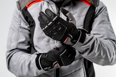 Motociclista ajustando guantes Xplorer negros para moto, ideales para aventura y turismo