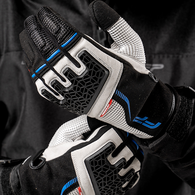 Guantes Xplorer gris con diseño robusto y ventilación inteligente para pilotos de aventura Guantes Xplorer gris para moto con detalles azules y negros, ideales para aventuras off-road y rutas extremas