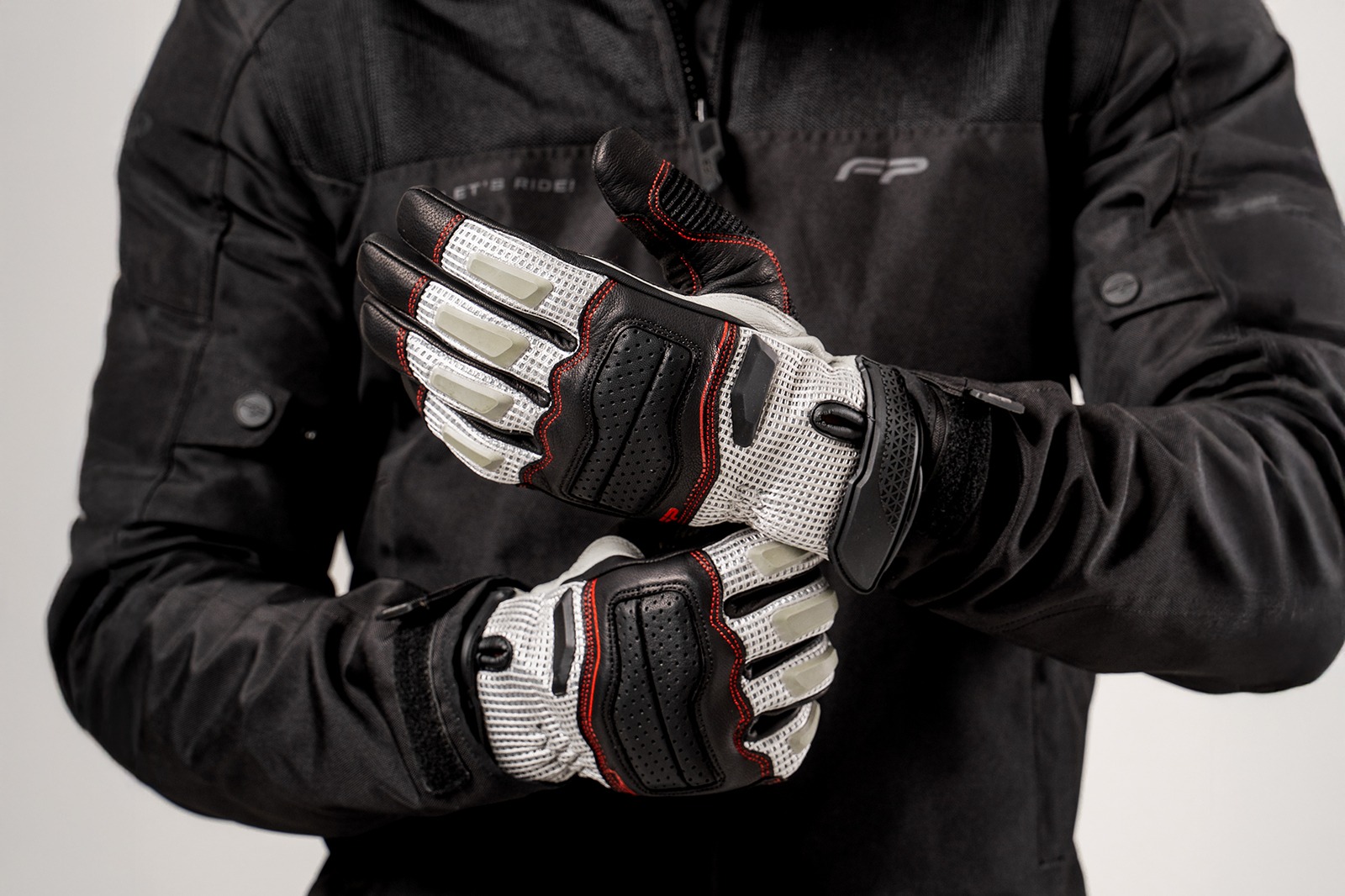 Motociclista ajustando guantes de cuero Asphalt Gris con malla ventilada y refuerzo en nudillos, ideales para conducción urbana y touring.