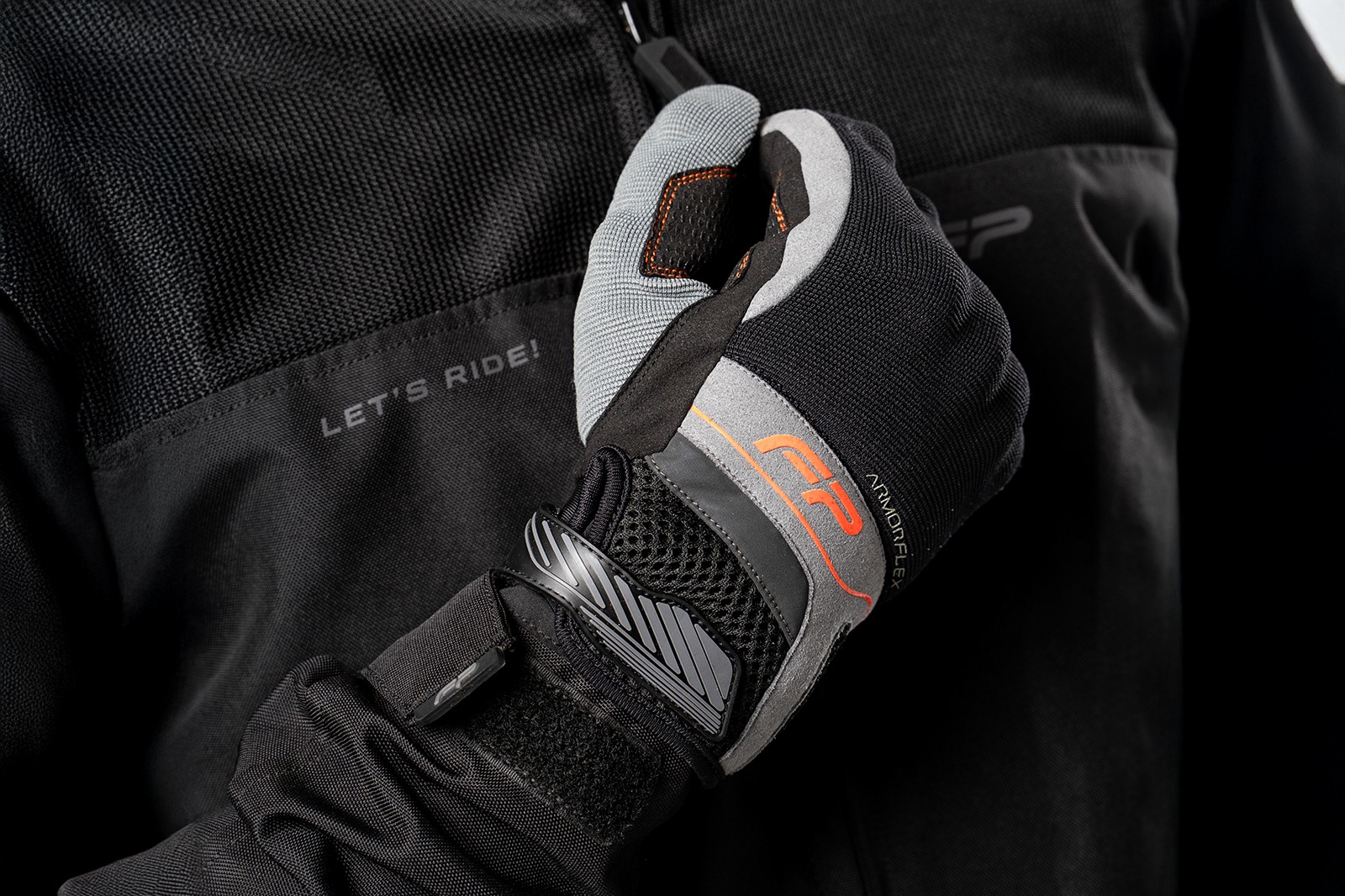 Motociclista ajustando cierre de guantes Core negros con detalles naranja, diseño seguro y cómodo para viajes en moto